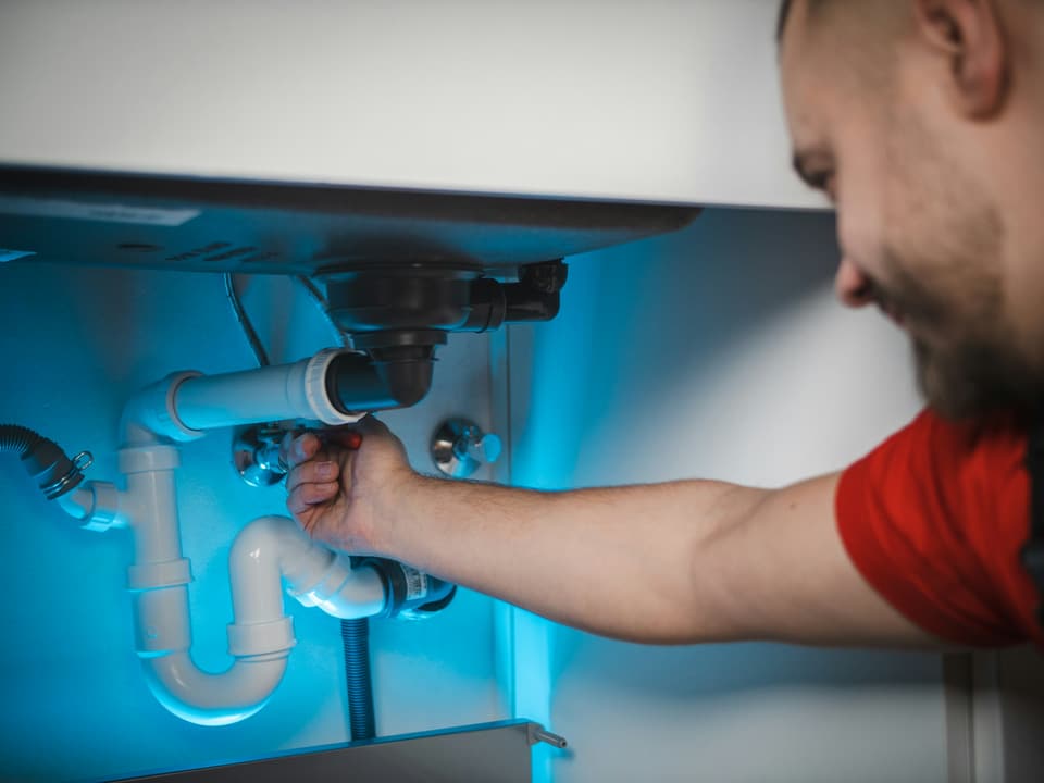 A man reaching under a sink to work on the white plastic drain trap